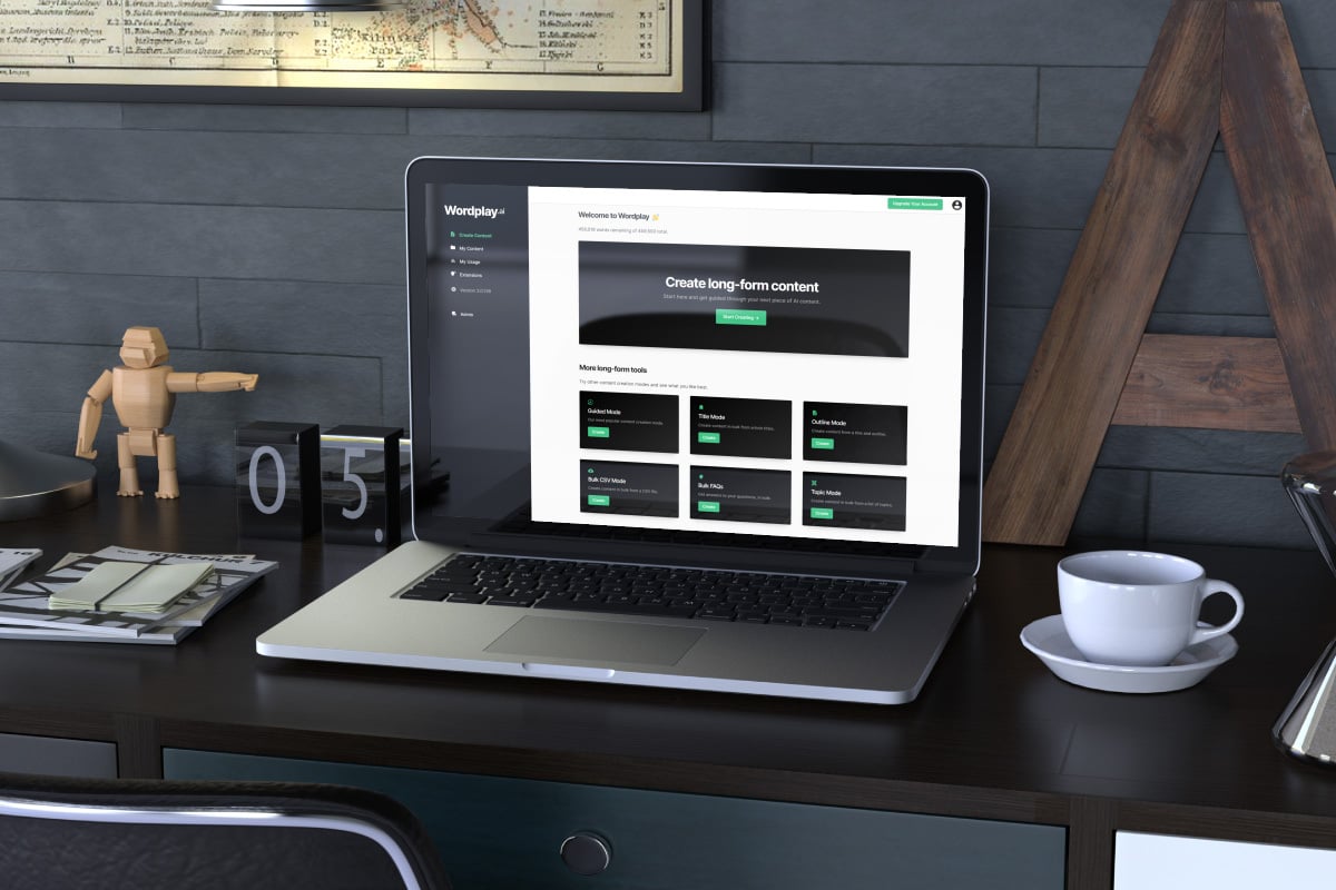 laptop with the wordplay app on screen is on top of the desk next to a coffee cup and a 3-d model figurine
