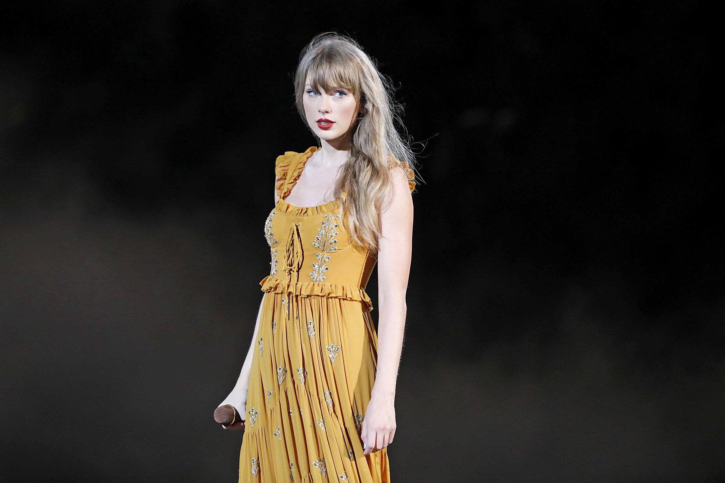 Taylor Swift in a yellow dress standing on stage of The Eras Tour