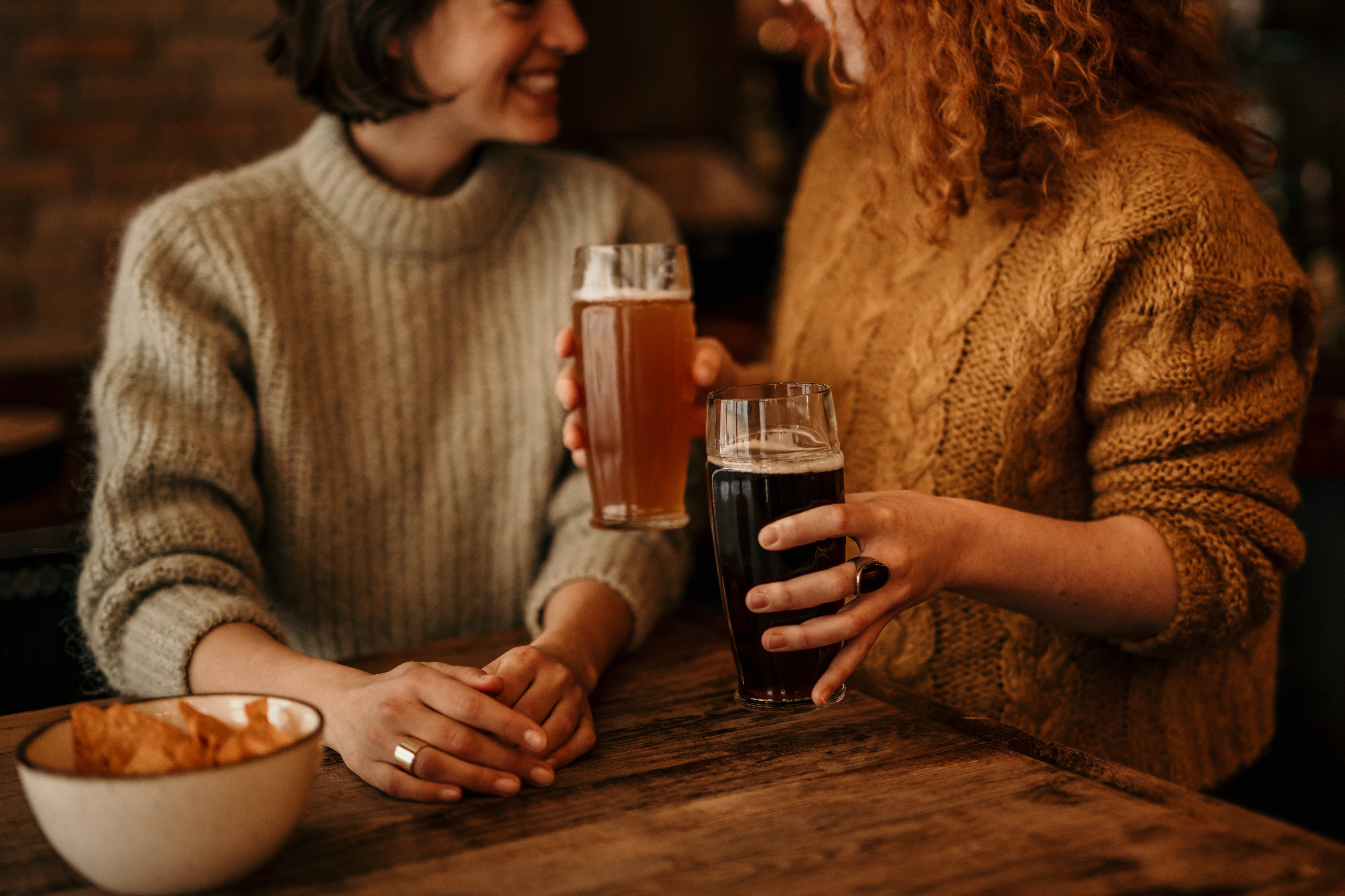 two women in sweaters with beers and chips at a pub table