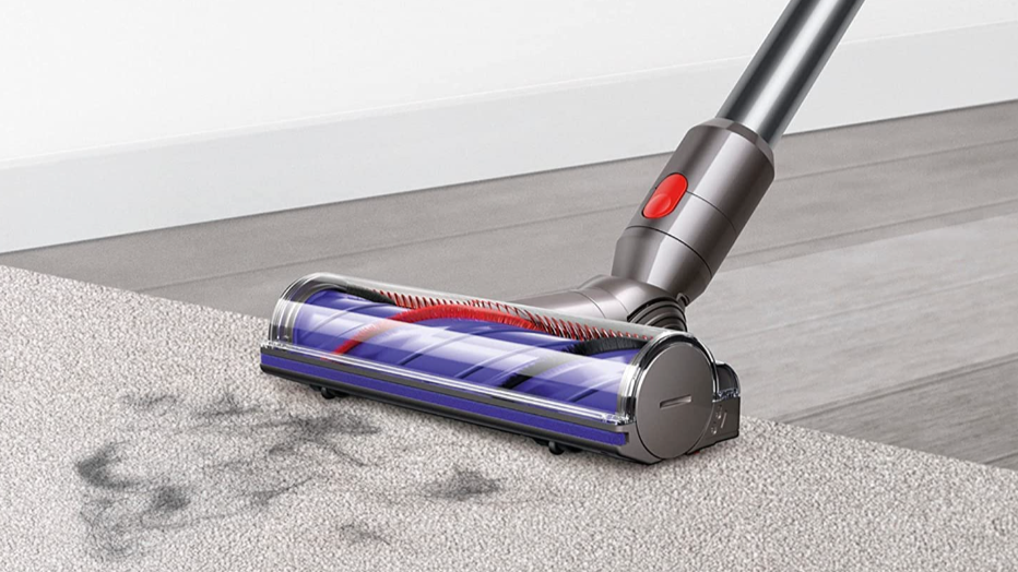 Dyson vacuum sweeping debris off a beige carpet
