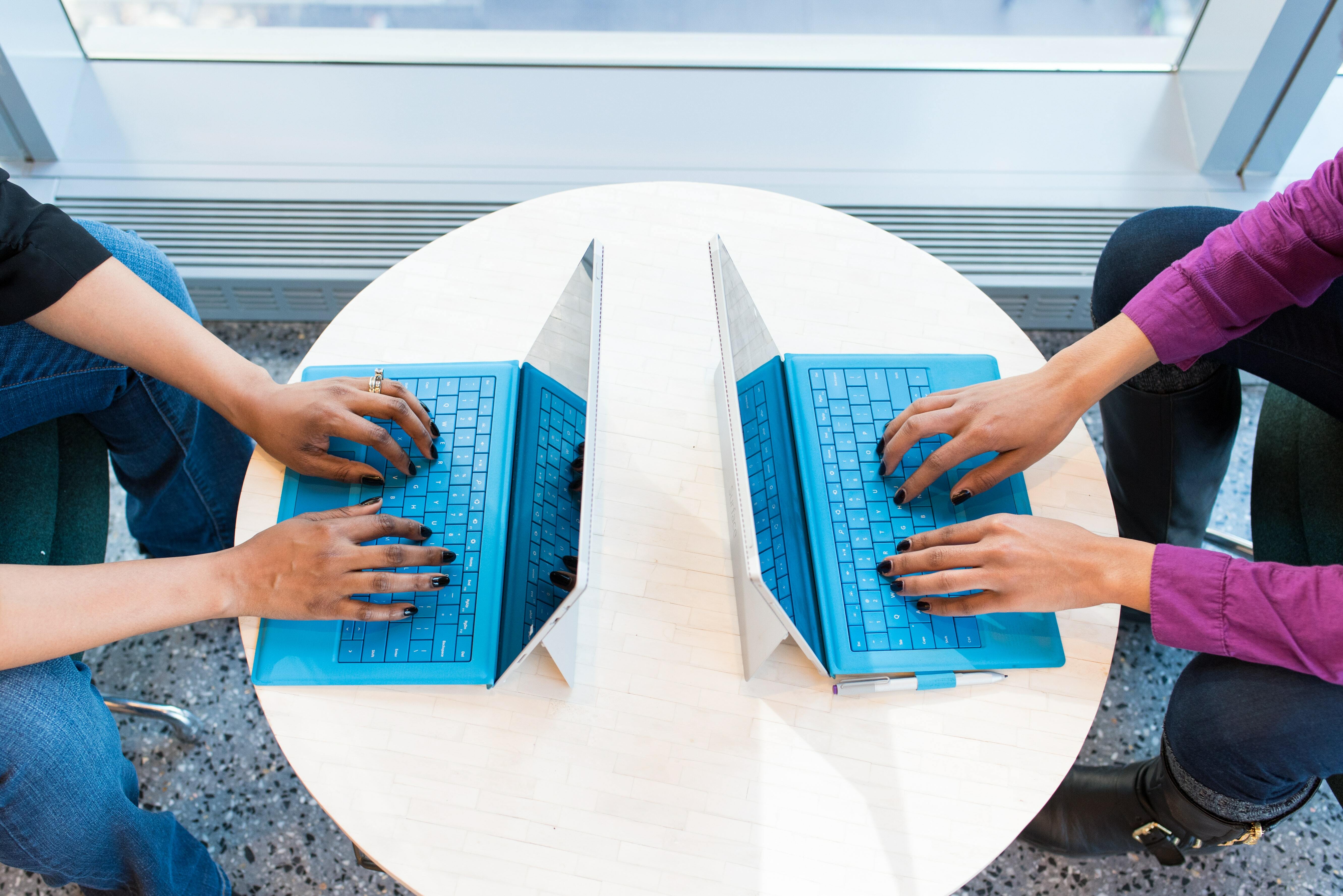 Two pairs of hands working on laptops
