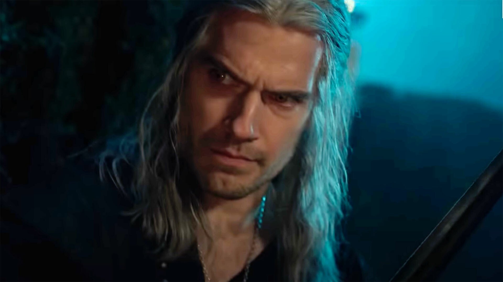 A man with long hair and a sword stands in the darkness.