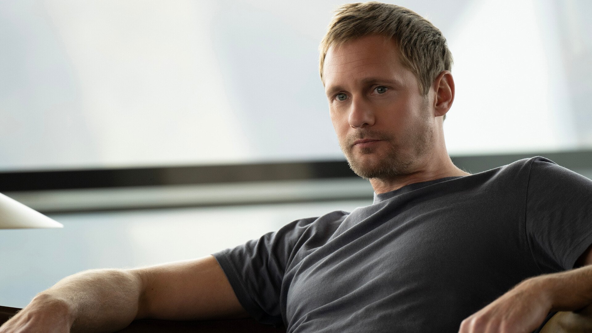 A man wearing a gray shirt sits on a couch.