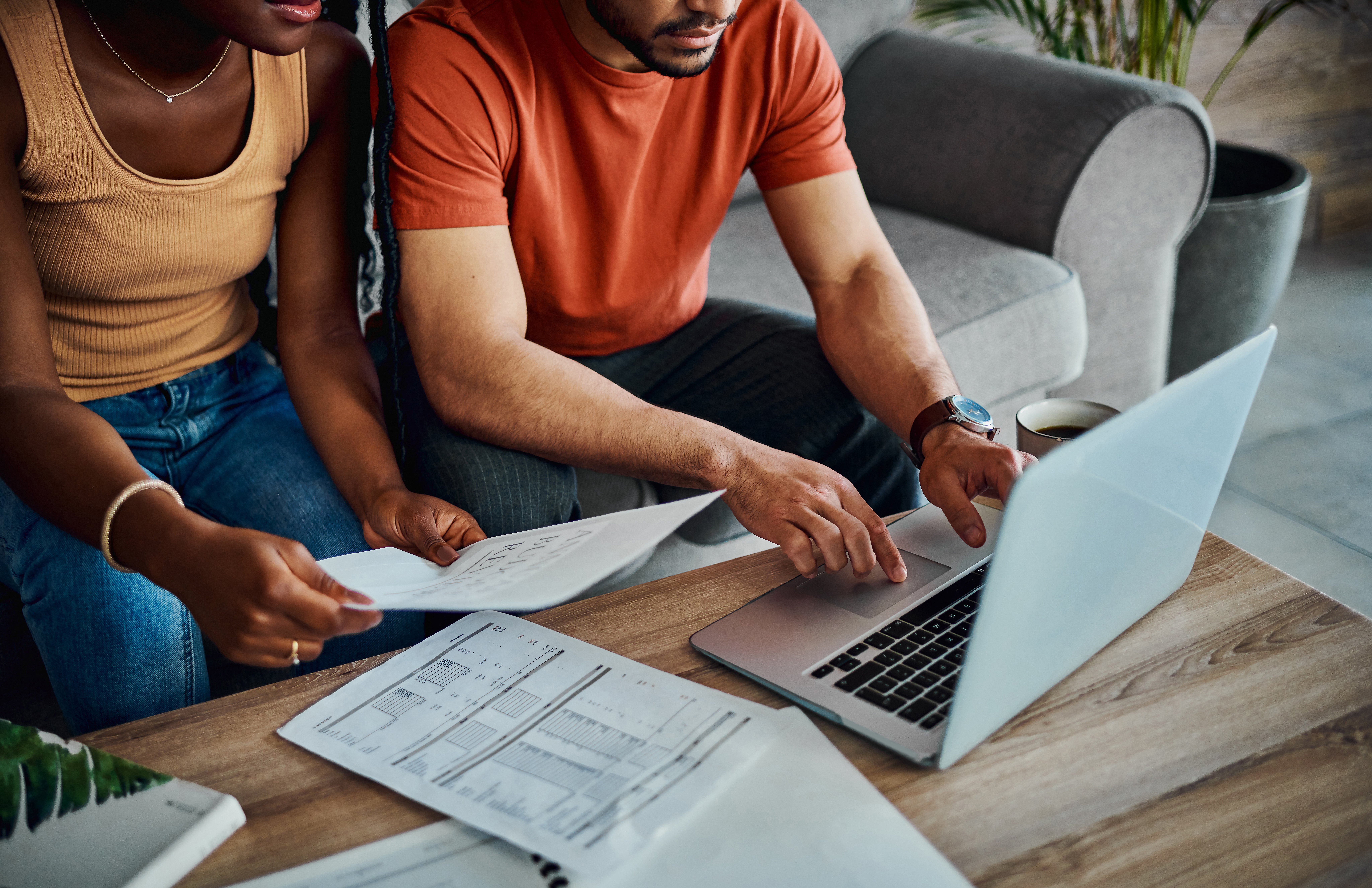 Cropped shot of a Black couple sitting in the living room and using a laptop to calculate their finances