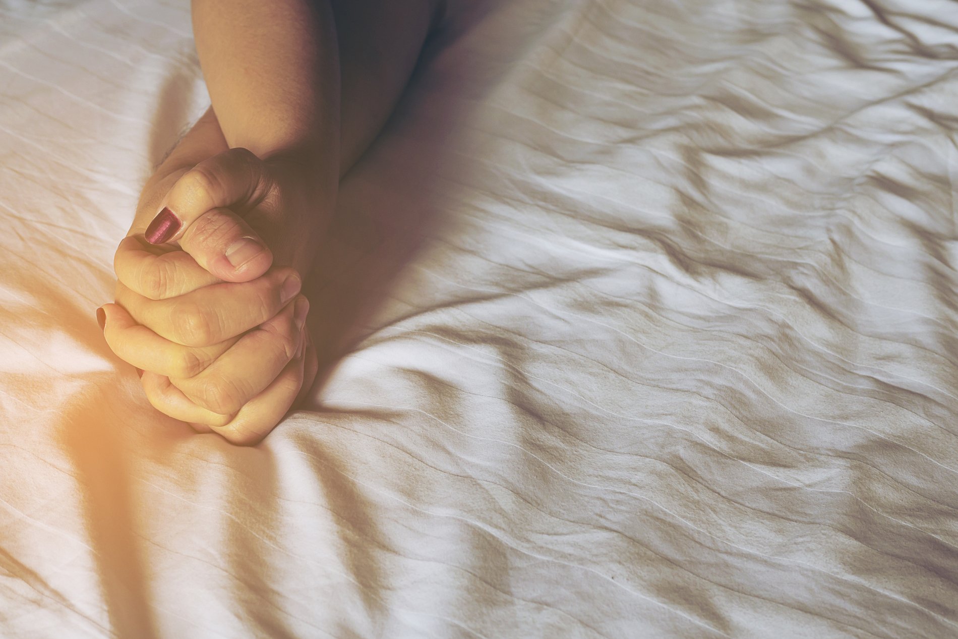 Close-Up Of Intimate Couple On Bed At Home with hands entwined.