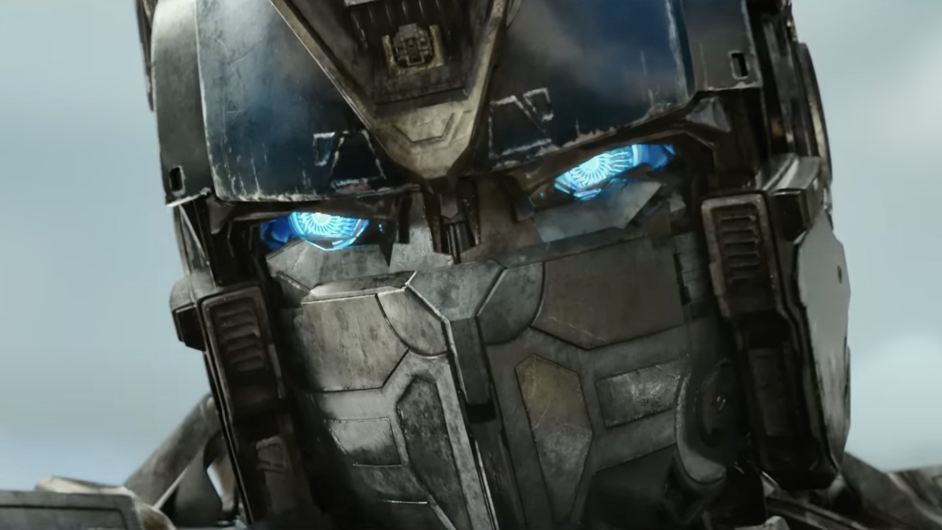 A close-up of the face of a giant metal robot with glowing blue eyes.
