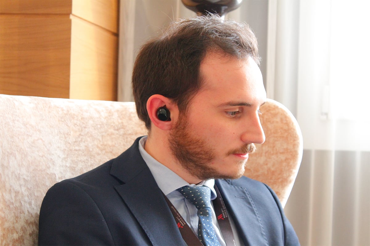 man is sitting down, looking to his left, with translator earbuds in his right ear
