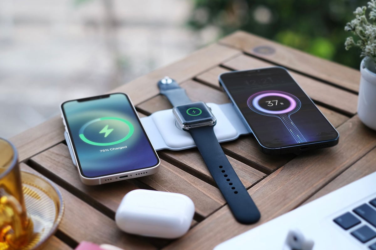 foldable charging station is laid out on a wooden table, with two iphones and a smartwatch being powered up
