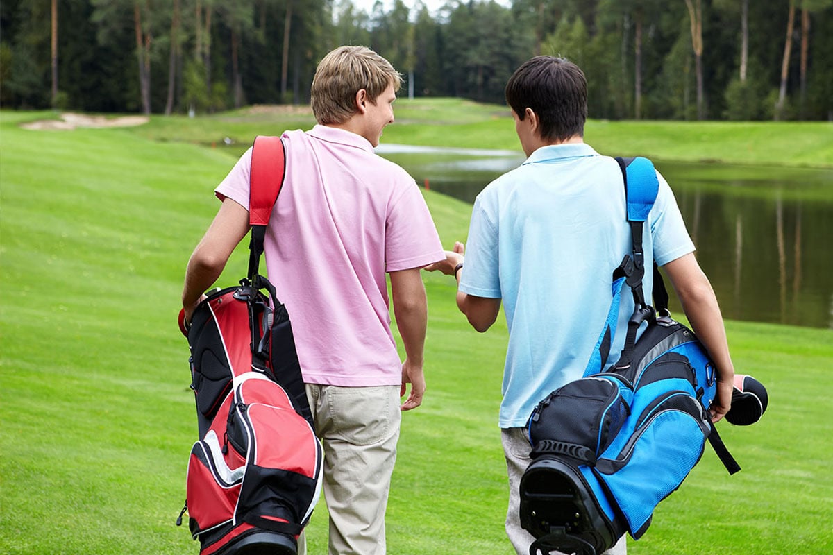 A man in a pink shirt walking on a golf course with a man in a blue shirt