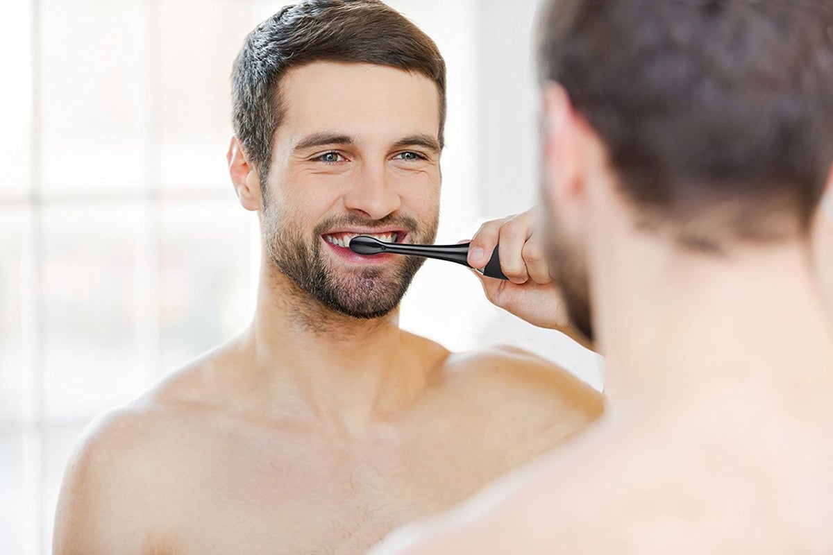 Man brushing his teeth in a mirror.