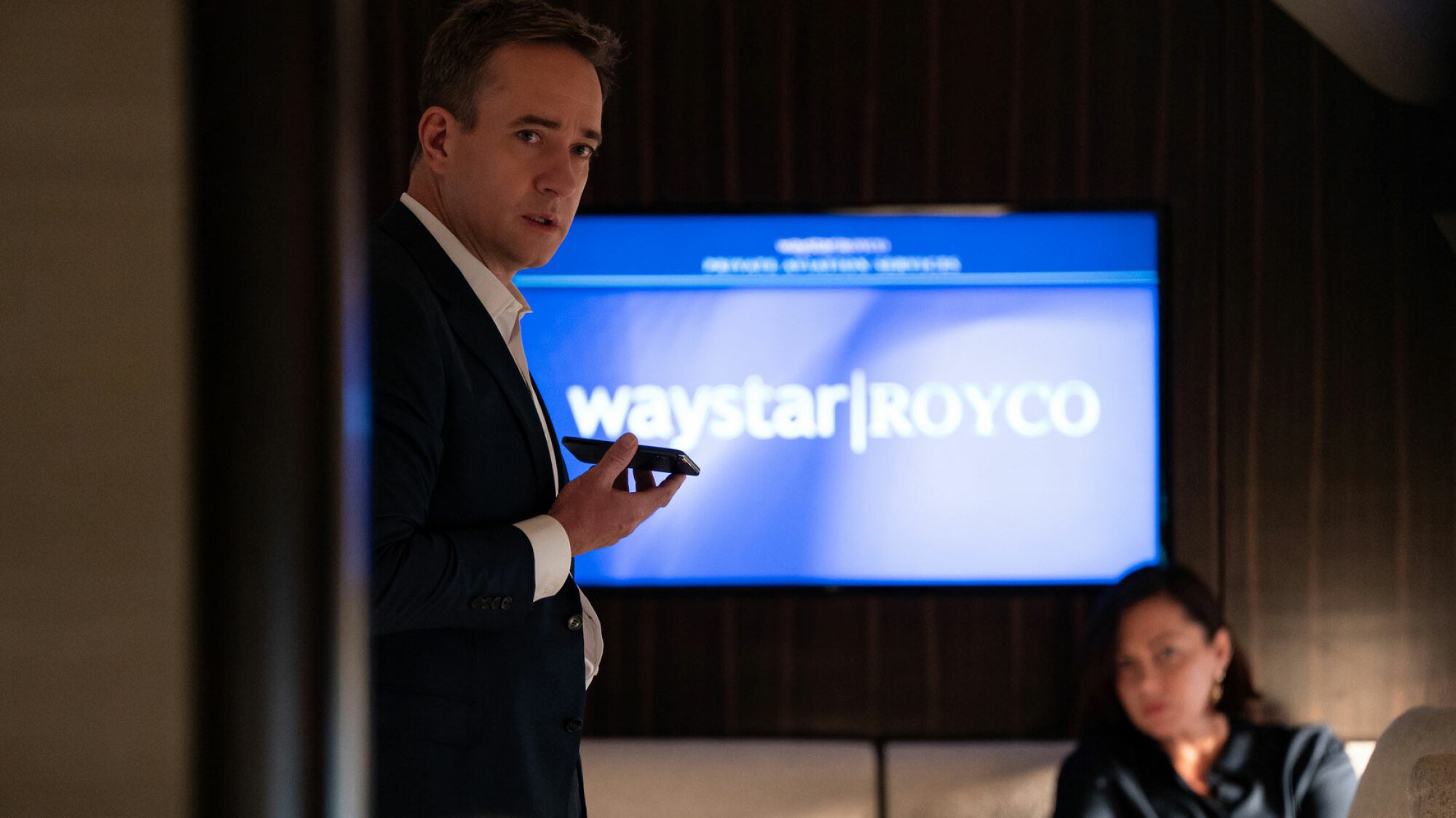 A man stands in a room on a private jet looking serious.
