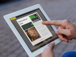 two hands are holding onto an ipad tablet with the learning software on screen, one hand is pointing at the screen, the other is holding up the tablet