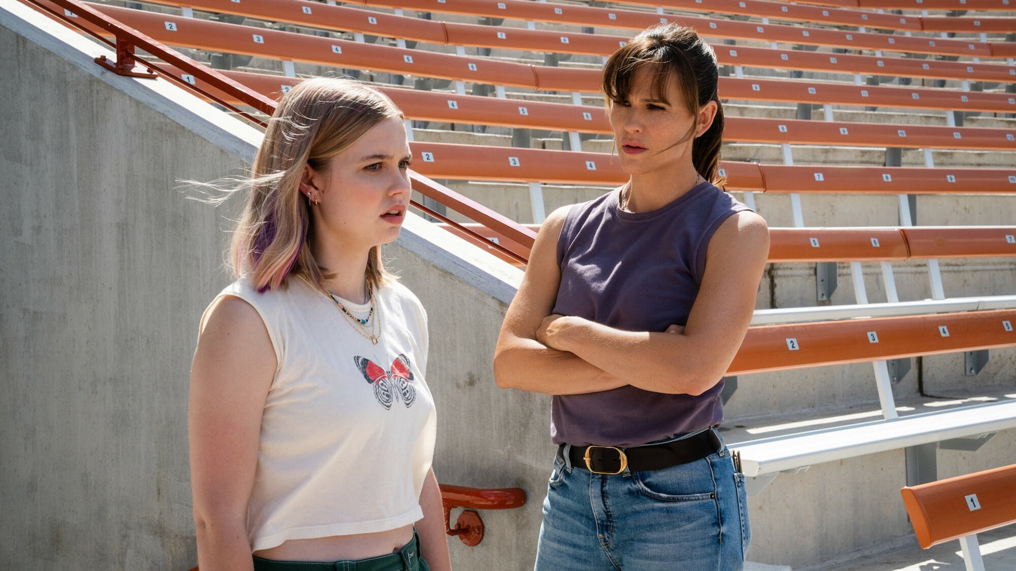 A teen and a woman stand in a school sports stadium.