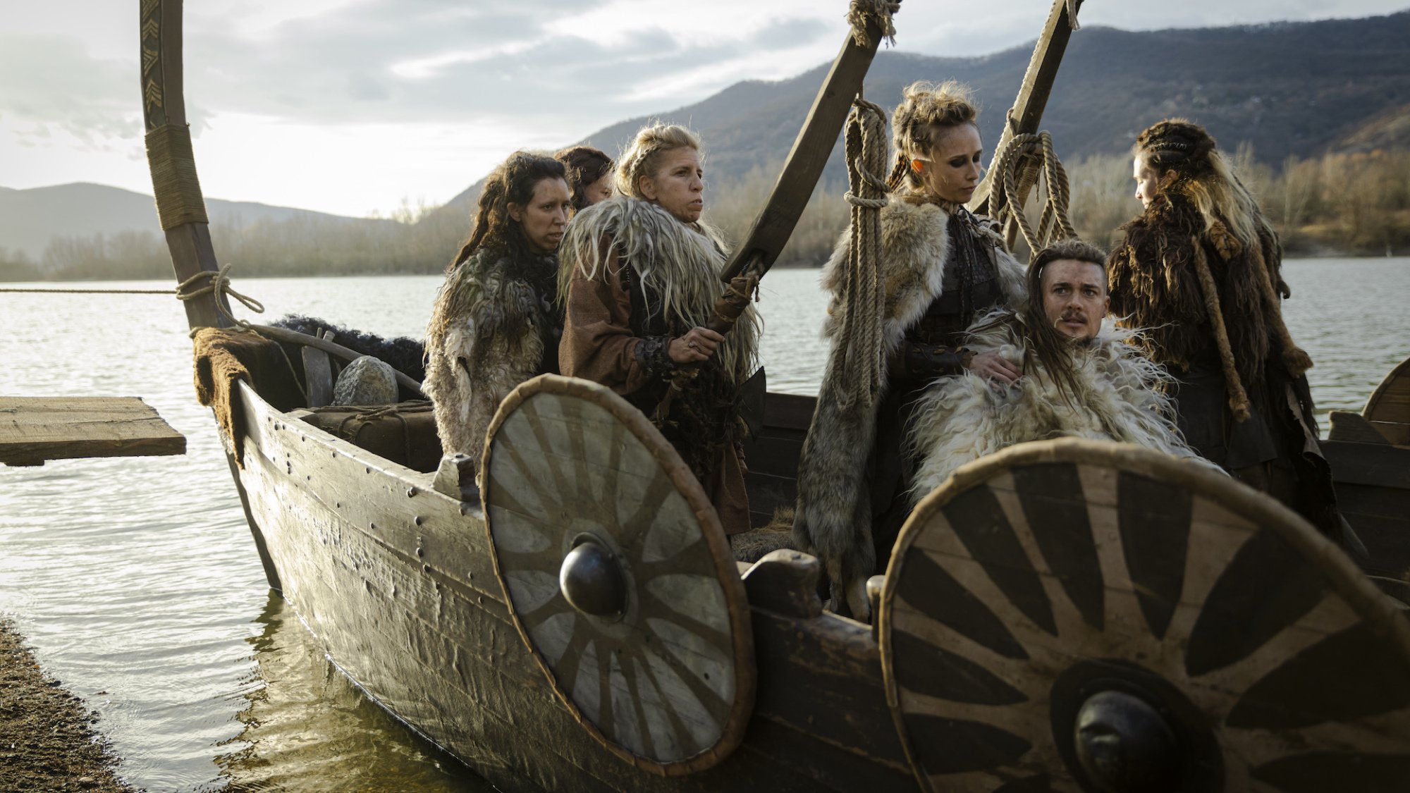 Vikings stand in a longboat at dawn.