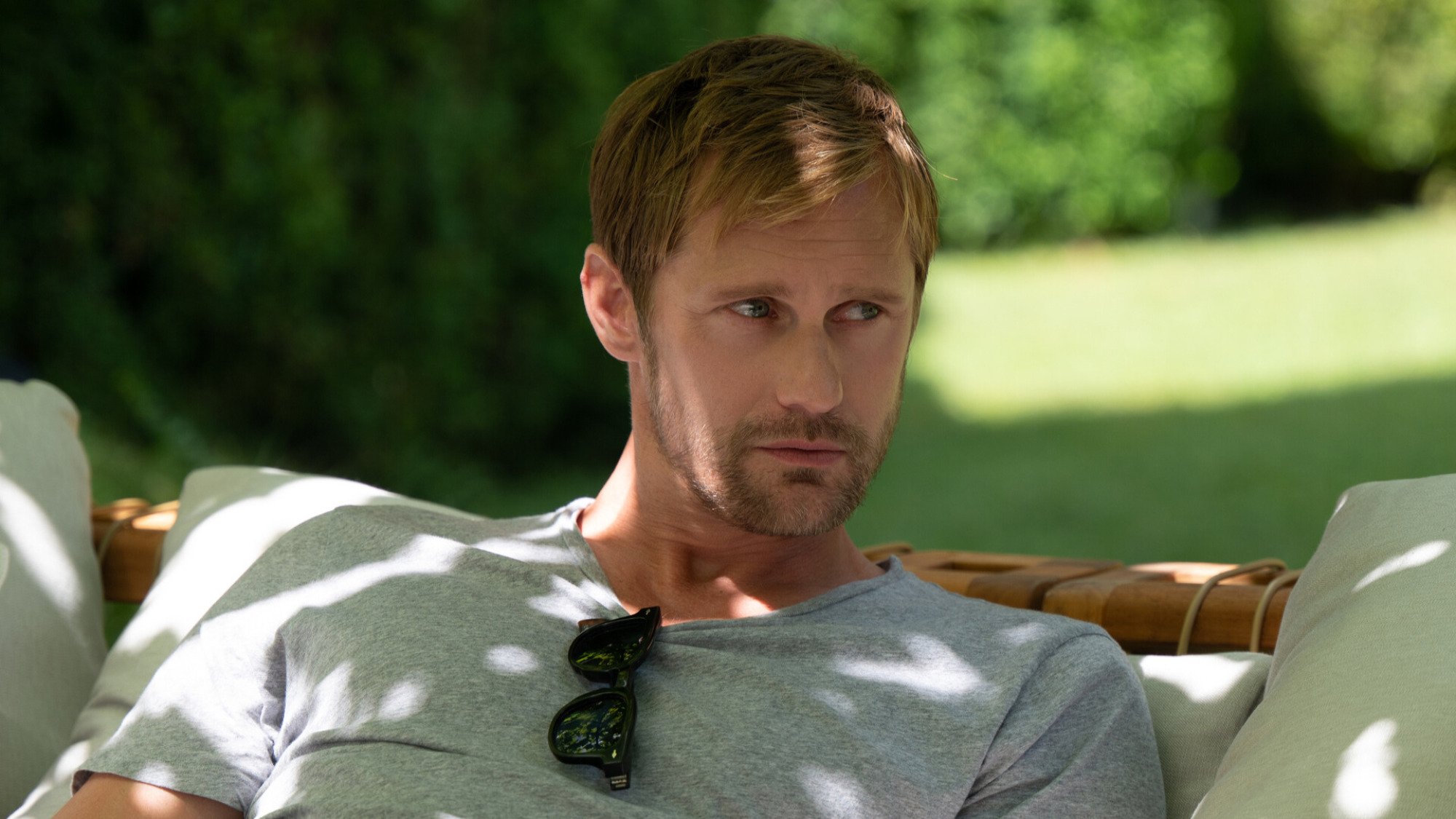 A man wearing a gray shirt lounges on a couch in a garden.