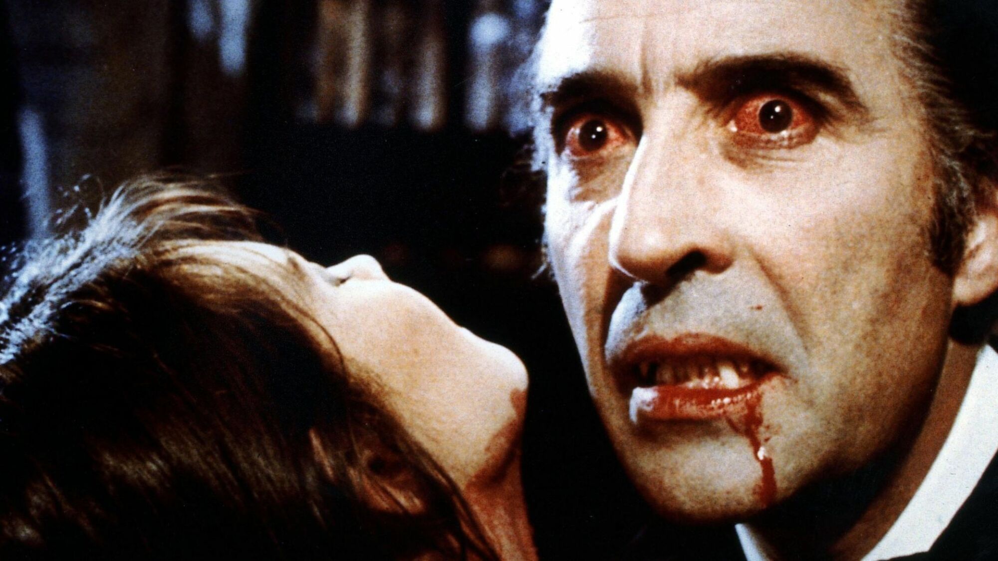 Christopher Lee plays Dracula with blood running down his chin and a woman in the foreground.