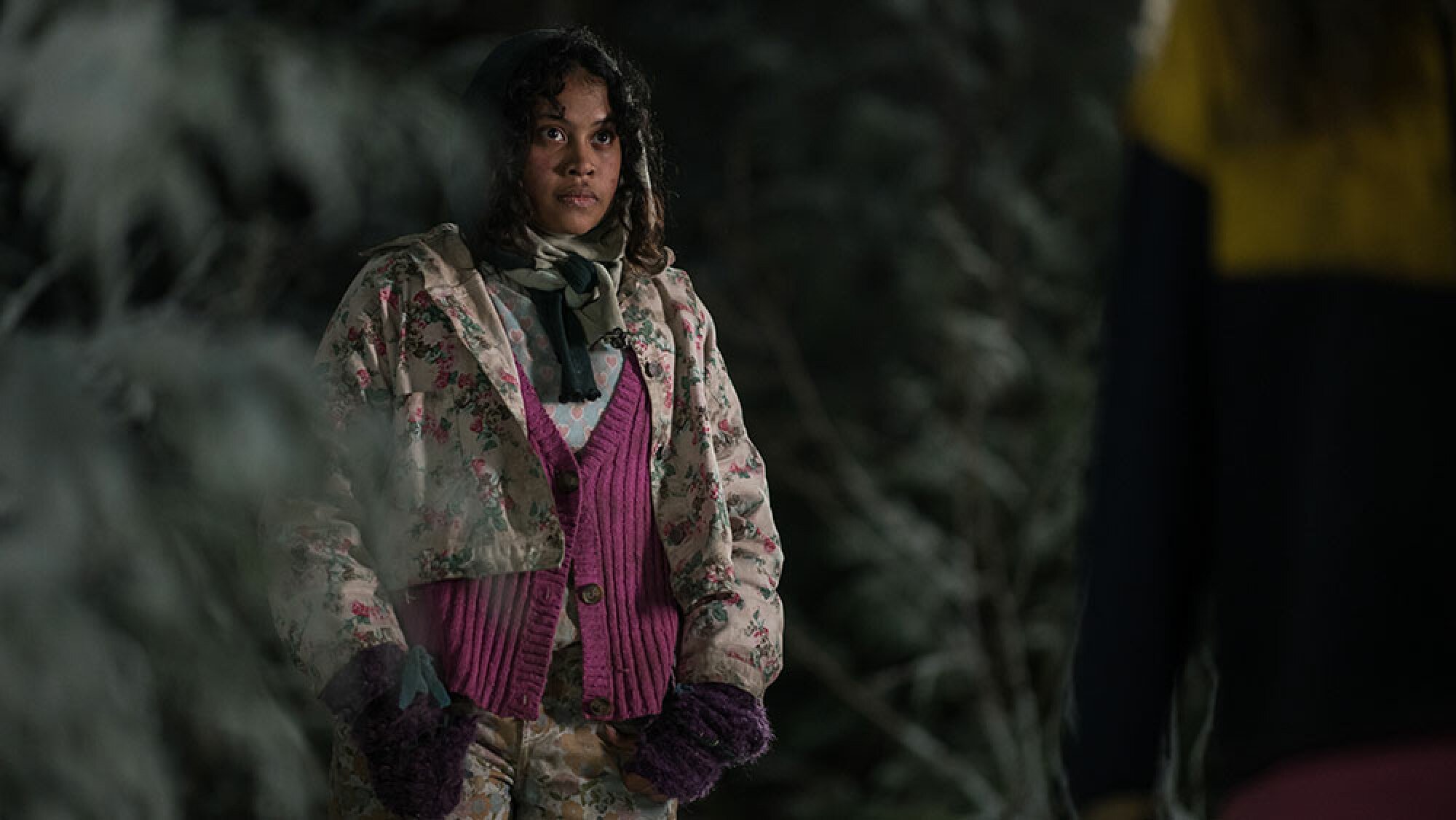 A woman with purple gloves and a white coat stands in the snowy wildnerness.
