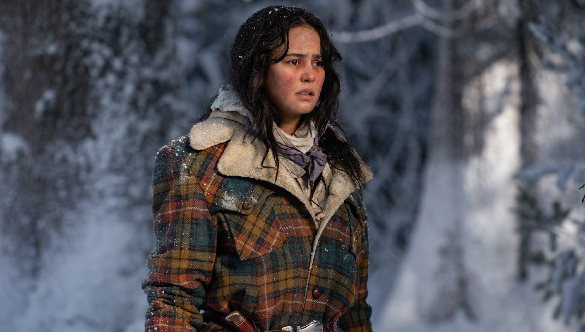 A girl stands in the snow bundled up but looking weary.