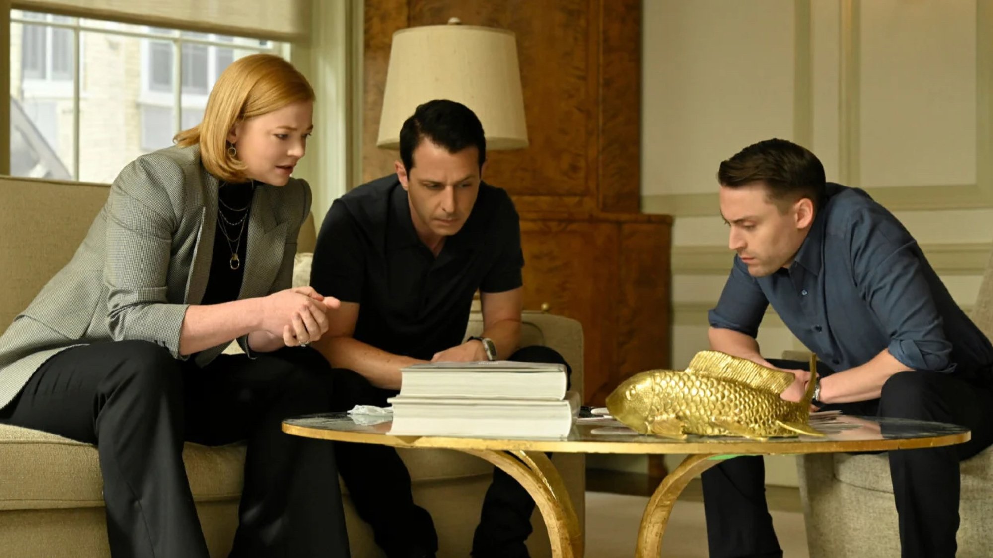 A woman and two men sit around a glass coffee table in an upscale living room.