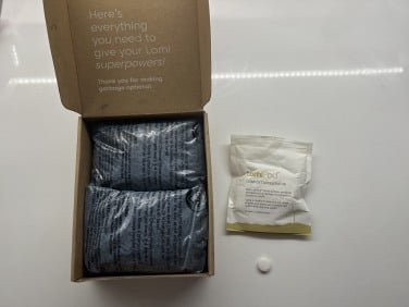Open cardboard box with bags of charcoal and bag of Lomi Pods on countertop
