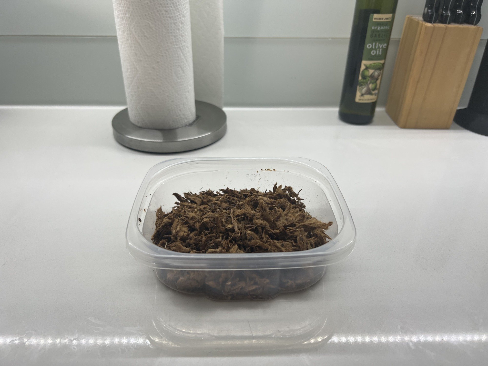 Plastic container filled with compost dirt on countertop with kitchen supplies in background