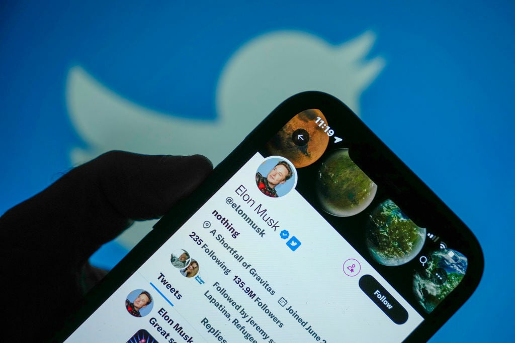 Elon Musk twitter profile on phone screen in front of Twitter logo