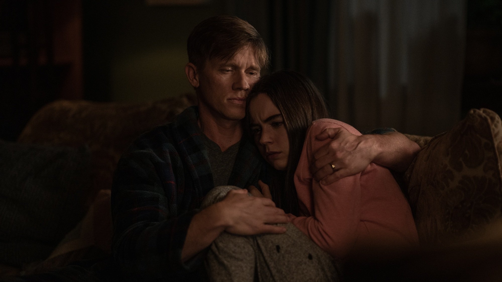 A man and his teenage daughter hug on a couch.