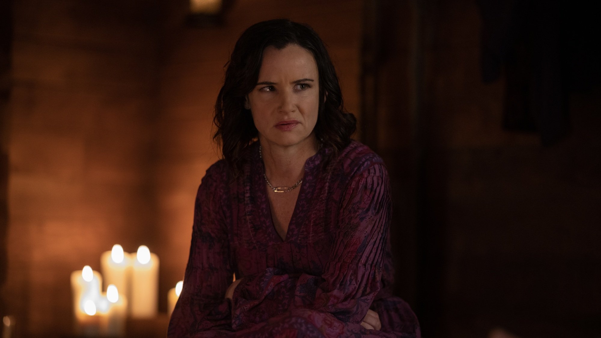A woman in a purple shirt sits in front of lit candles.