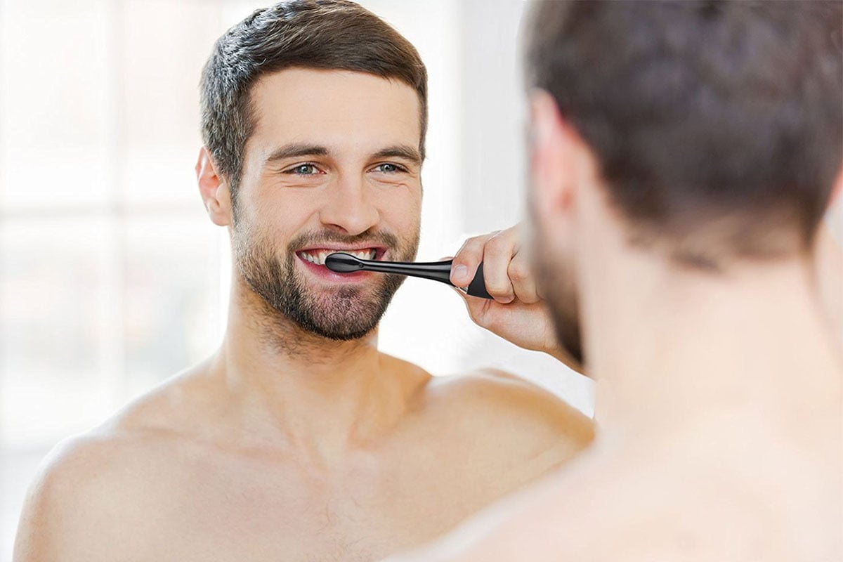 Man using Aquasonic black toothbrush in front of mirror.
