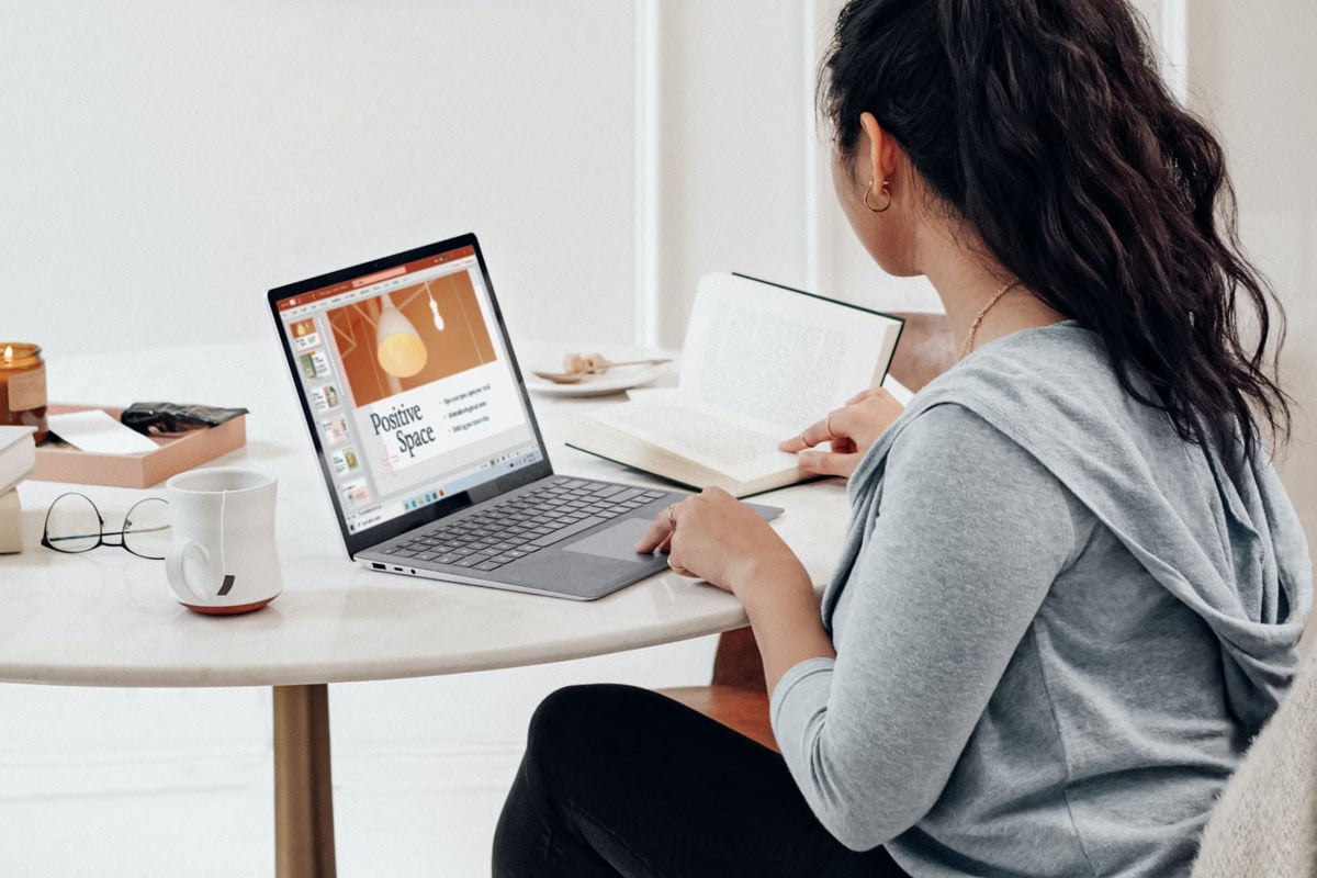 Woman working on laptop at a table with a cup of tea nearby.