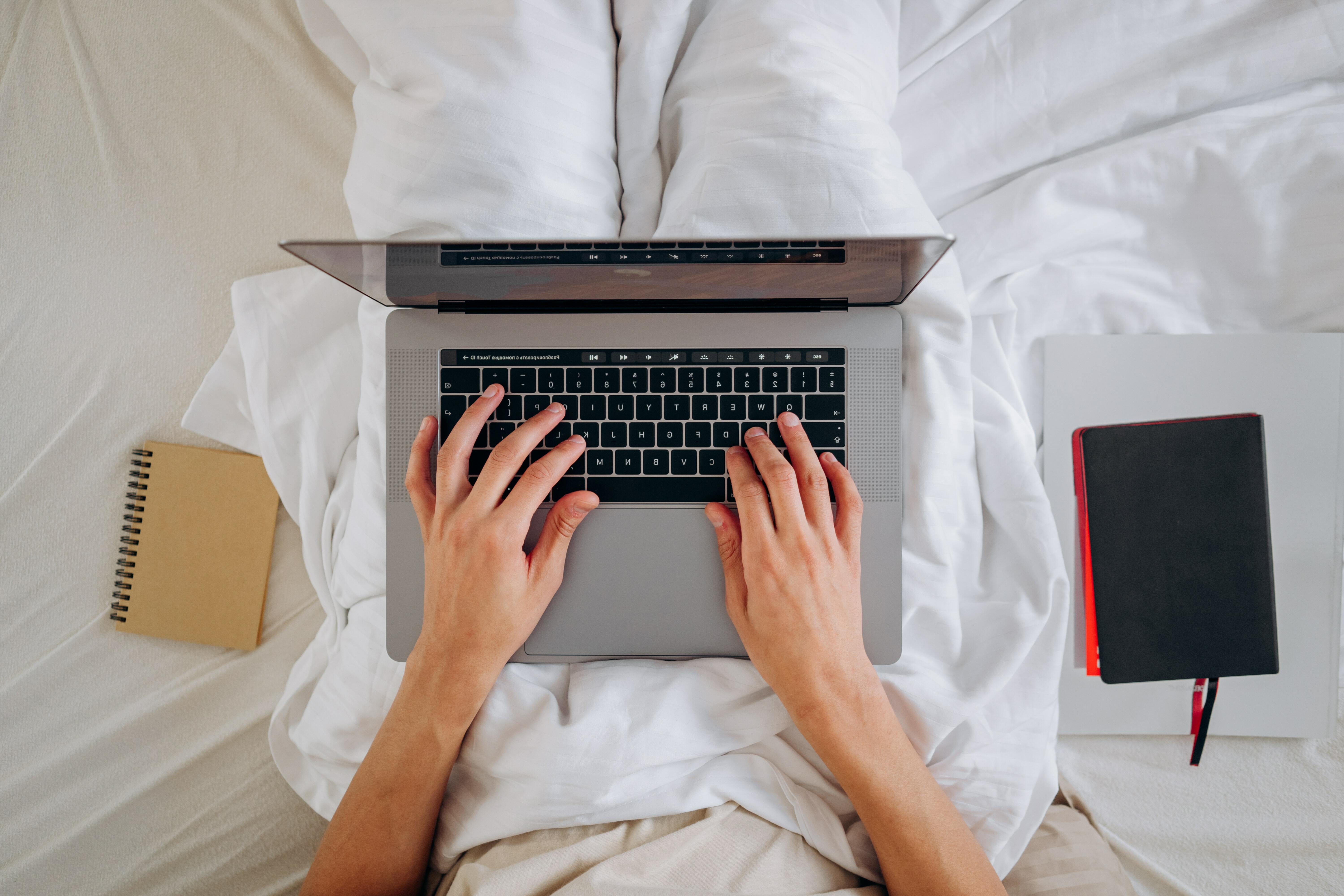 person typing on laptop in bed