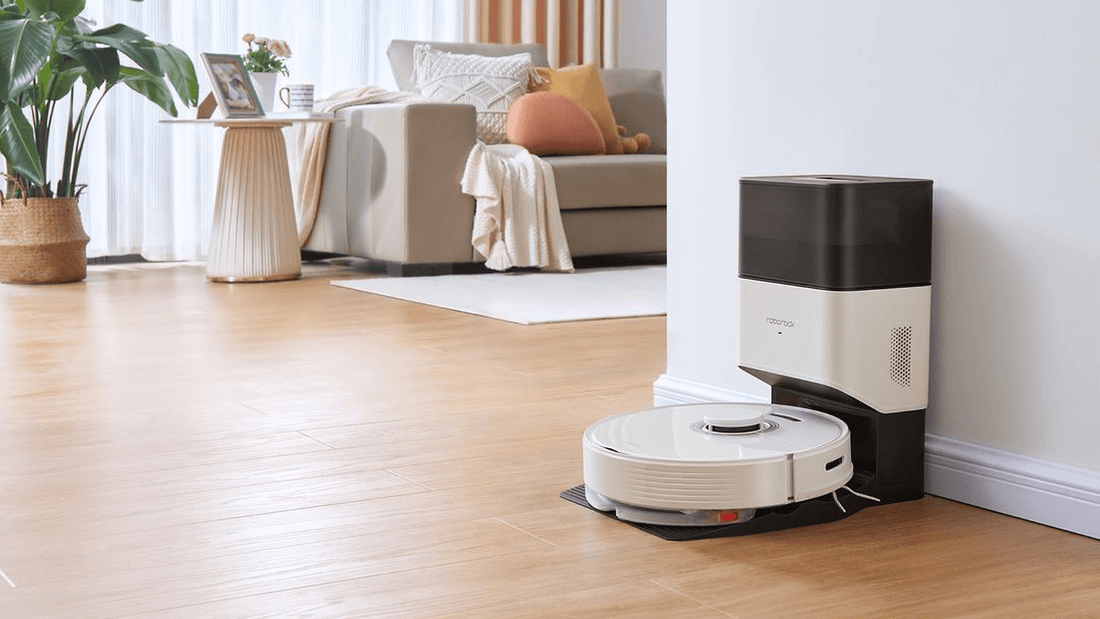 White Roborock vacuum and dock sitting against wall with living room furniture in background