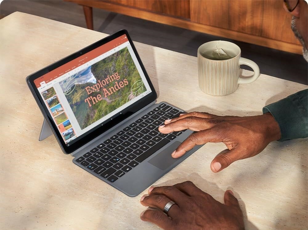 a person uses the amazon fire max 11 tablet with a keyboard while sitting at a table. a white mug of tea sits off to the right of the tablet with keyboard