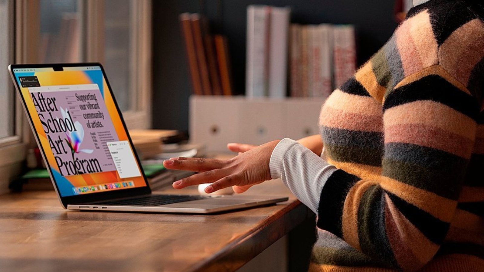 a close-up of a woman in striped sweater typing on a 15-inch m2 apple macbook air at a wooden table