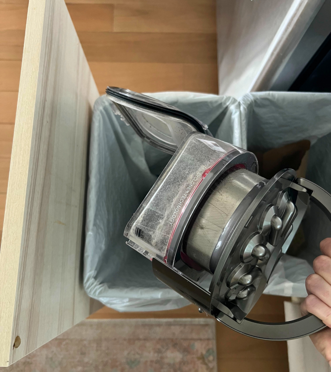 Hand holding Dyson robot vacuum dust bin over trash can