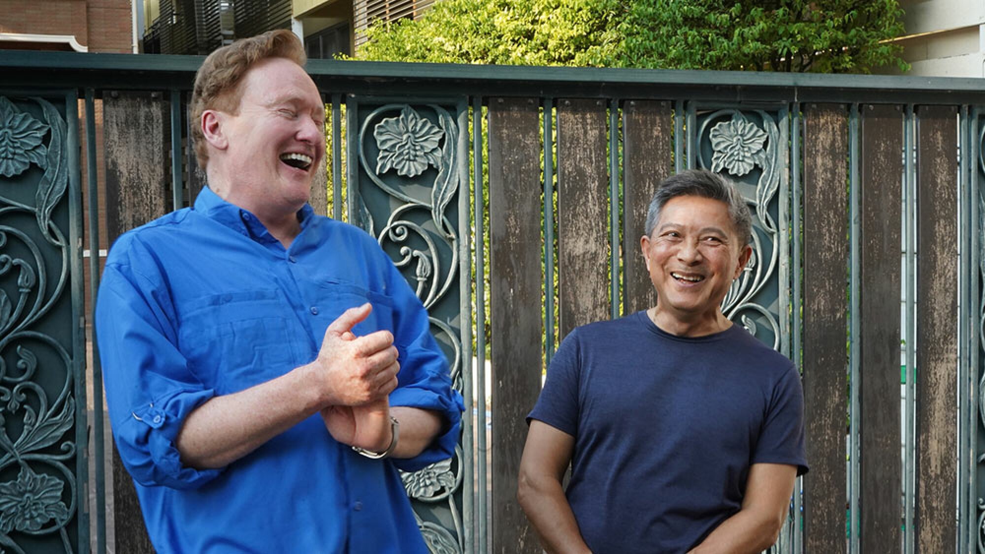 A man stands with another man, laughing.