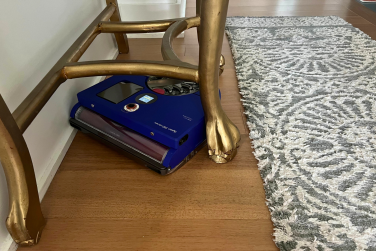 Dyson 360 Vis Nav robot vacuum cleaning hardwood floor in between gold table legs