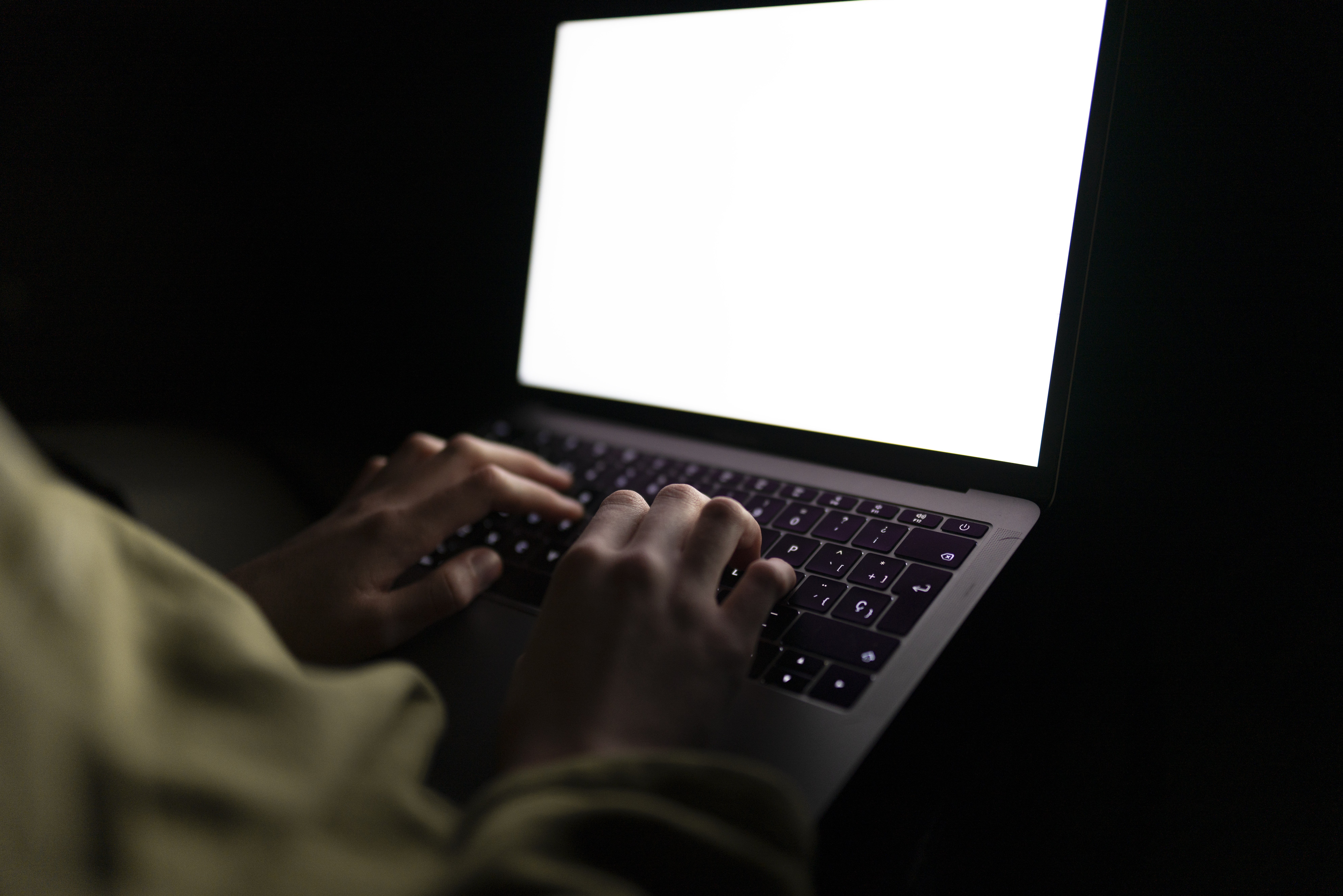 A pair of hands typing on a laptop in the dark.