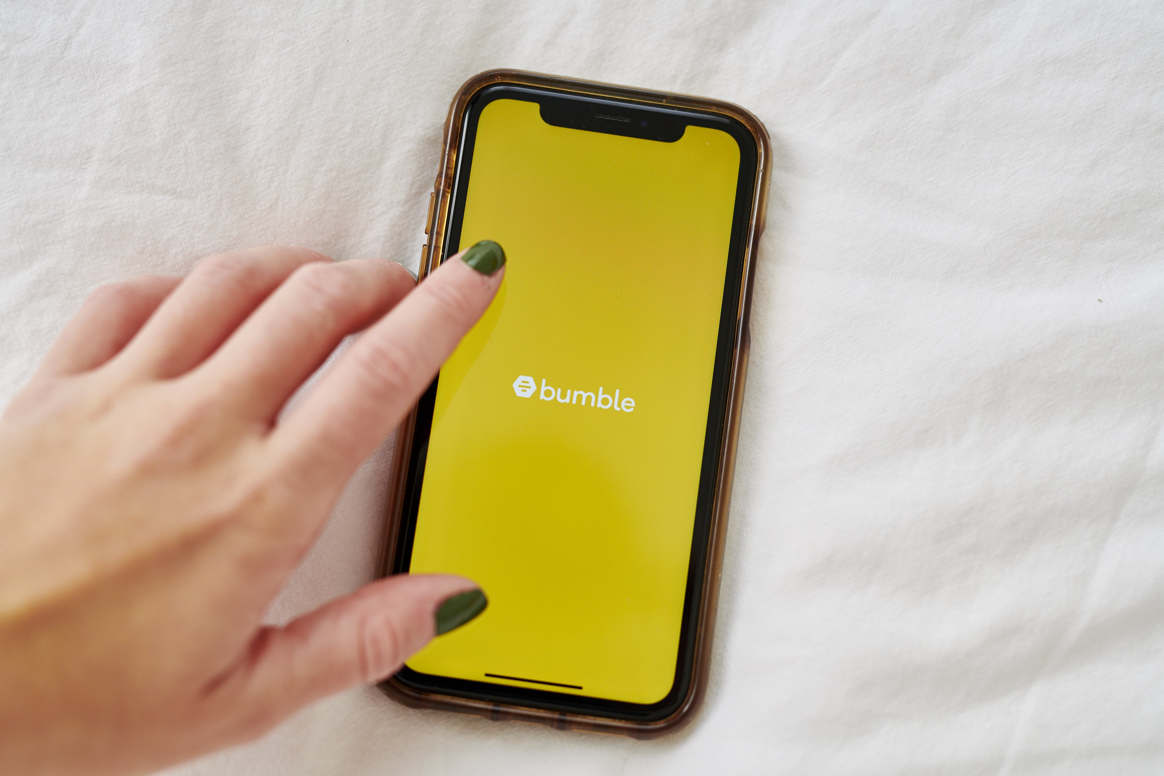 A hand over a smartphone displaying the Bumble logo. 