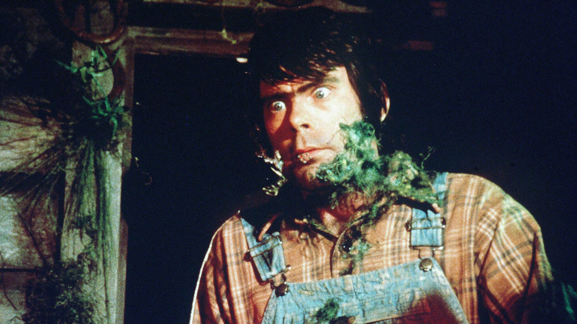 A man in overalls has a green growth on his face.