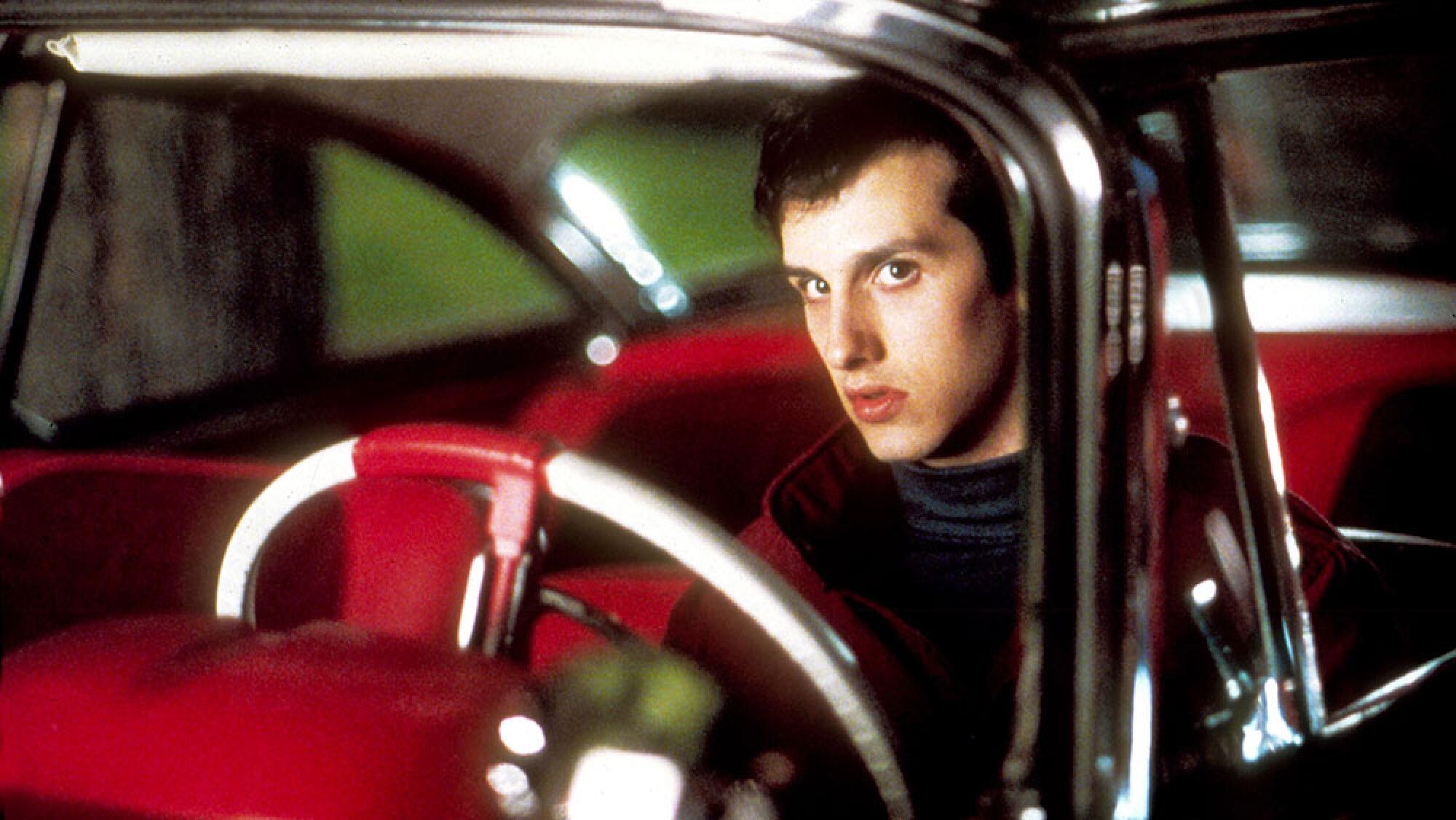 A young man sits in a red 1958 Plymouth Fury car.