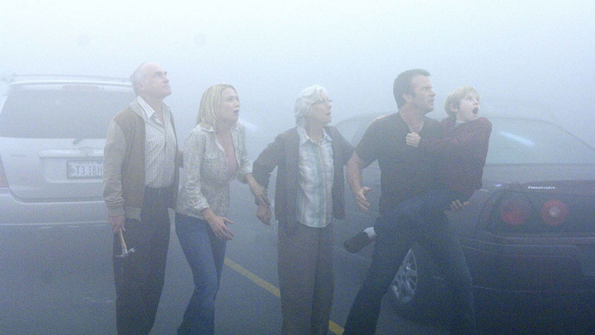 A group of people stand in a misty carpark.