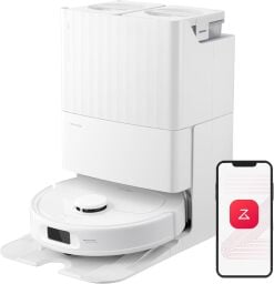 A white robot vacuum appears in its dock next to a smart phone on a white, blank background.