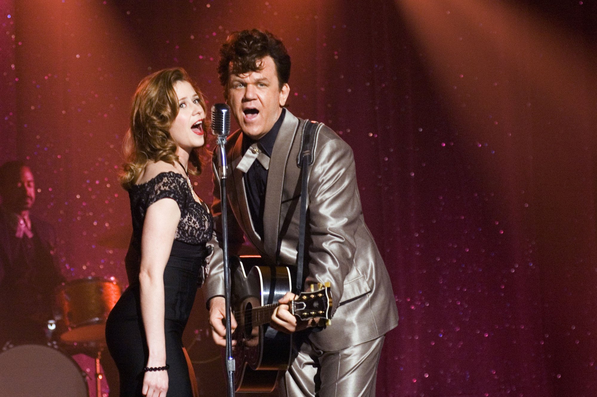 Jenna Fischer and John C. Reilly singing into an old-fashioned mic on stage in a still from "Walk Hard."